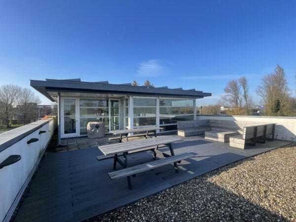 Dakterras met houten zitbanken en picknicktafels aan de Jan Leentvaarlaan, bij een modern gebouw met glazen gevel.
